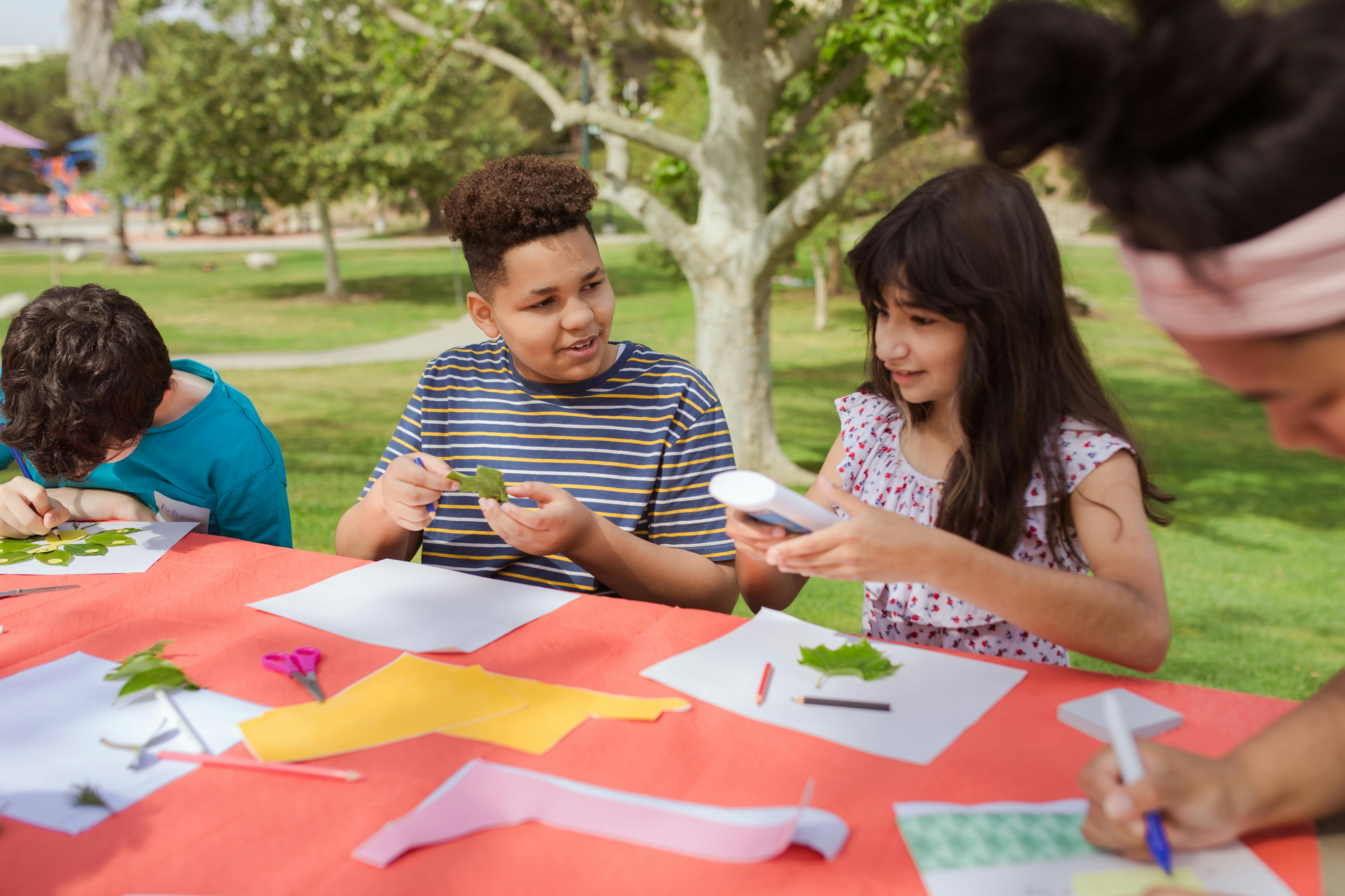 Children making crafts with leaves and glue at an outdoor table